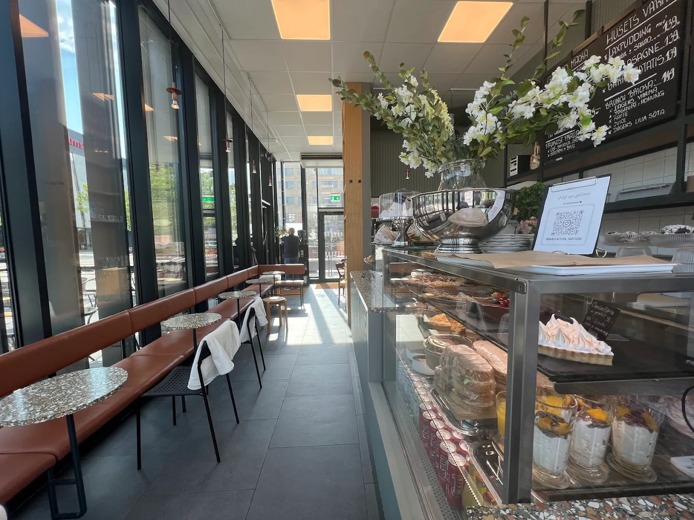 A long bench with tables in front of a showcase cabinet with pastries and yoghurt cups